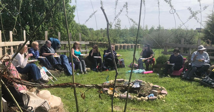group of people sat around campfire eating outdoors at Dalton Moor Farm during the day